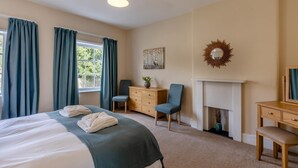 Een hotelkamer met een bed, twee stoelen, een kaptafel, een spiegel en een open haard.