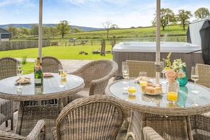 Eine Terrasse mit Korbmöbeln, einem Whirlpool und einem schönen Blick auf ein grünes Feld und Hügel.