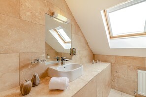 Ein modernes Badezimmer mit Dachfenster, einem großen Spiegel, einem freistehenden Waschbecken und dekorativen Vasen.