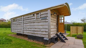 Une cabane en bois avec une pancarte sur laquelle on peut lire « Gloyn Byw ». Elle est recouverte de bois à l’extérieur, possède un porche avec des marches et une petite fenêtre.