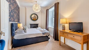 Hotelkamer met een bed, televisie, bureau, stoel, spiegel, open haard en raam met gordijnen.