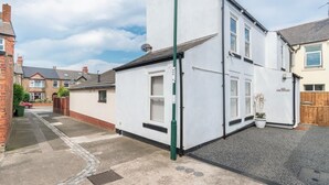 A residential street with houses, a white building with a green door, and a red car parked on the street. - 2 Bed in Saltburn-by-the-Sea (oc-cl004) (Saltburn-by-the-Sea)