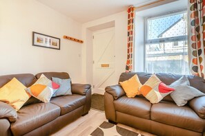 A living room with two brown leather sofas, a patterned rug, a framed picture on the wall, and a window with curtains. - 3 Bed in Ambleside (oc-w31932) (Ambleside)