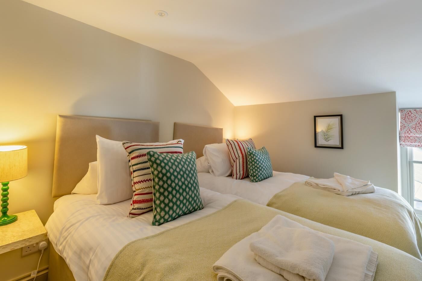 Quarto de hotel com duas camas, uma luminária de cabeceira e um quadro na parede.