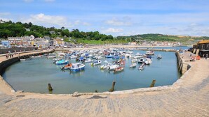 A harbor with numerous boats docked, a stone quay, and buildings in the background. - 3 Bed in Lyme Regis (oc-s31839) (Lyme Regis)