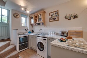 Eine kompakte Küche mit Herd, Backofen, Waschmaschine und Spüle. Oberhalb der Spüle befinden sich Schränke sowie ein Holzschrank mit Regalen.