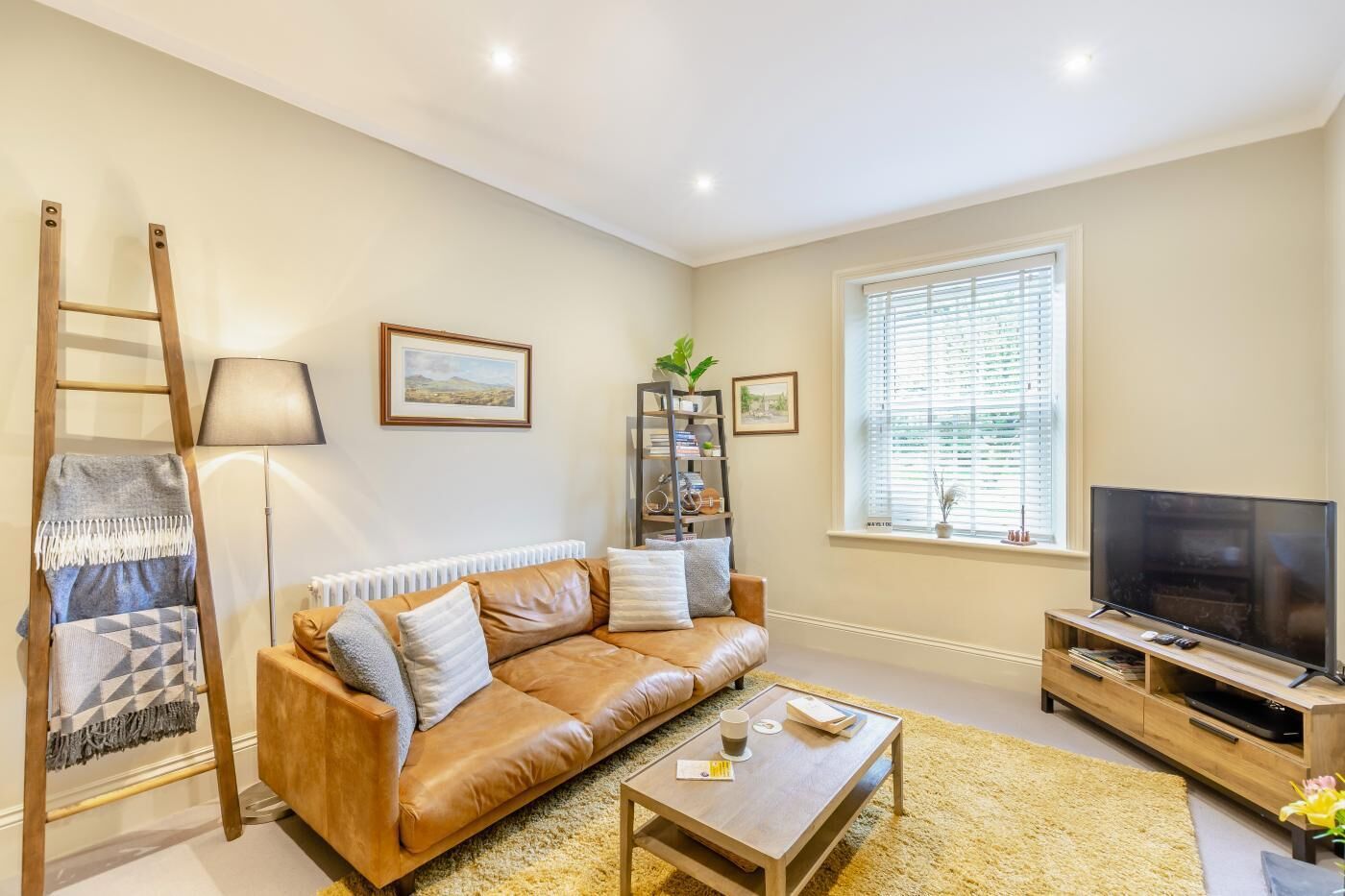 A living room with a sofa, a coffee table, a TV, a bookshelf, and a window with blinds.