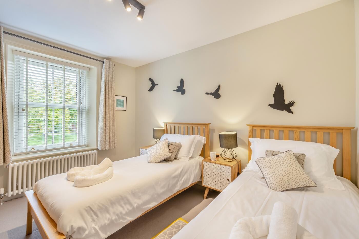 Een tweepersoonskamer met twee bedden, een raam met zonwering, een radiator en wanddecoratie van vogels.