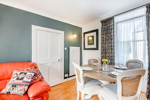A dining area with a round table, white chairs, and a red sofa with patterned cushions.