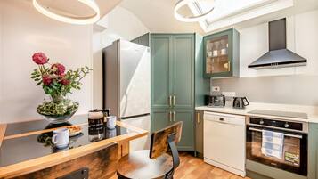 A modern kitchen with a dining area, featuring a refrigerator, oven, dishwasher, and a coffee machine.