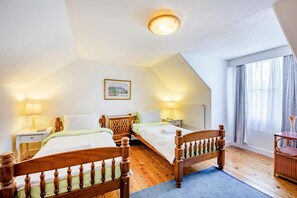Ein Hotelzimmer mit zwei hölzernen Betten, einer Deckenleuchte, einem Bild an der Wand und einem Fenster mit Vorhängen.