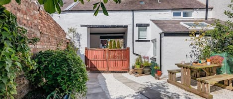 A residential property with a gravel pathway, a wooden gate, a patio table, and potted plants.