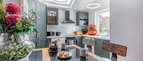 A modern kitchen with a glass-top table, a coffee maker, and a view of the city.