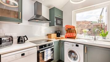 A compact kitchen with a dishwasher, oven, microwave, and a window with a view of the city.