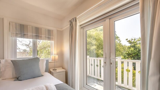 A hotel room with a bed, bedside table, lamp, and a view of a balcony with a railing. - 3 Bed in Reydon (oc-brae) (Reydon)