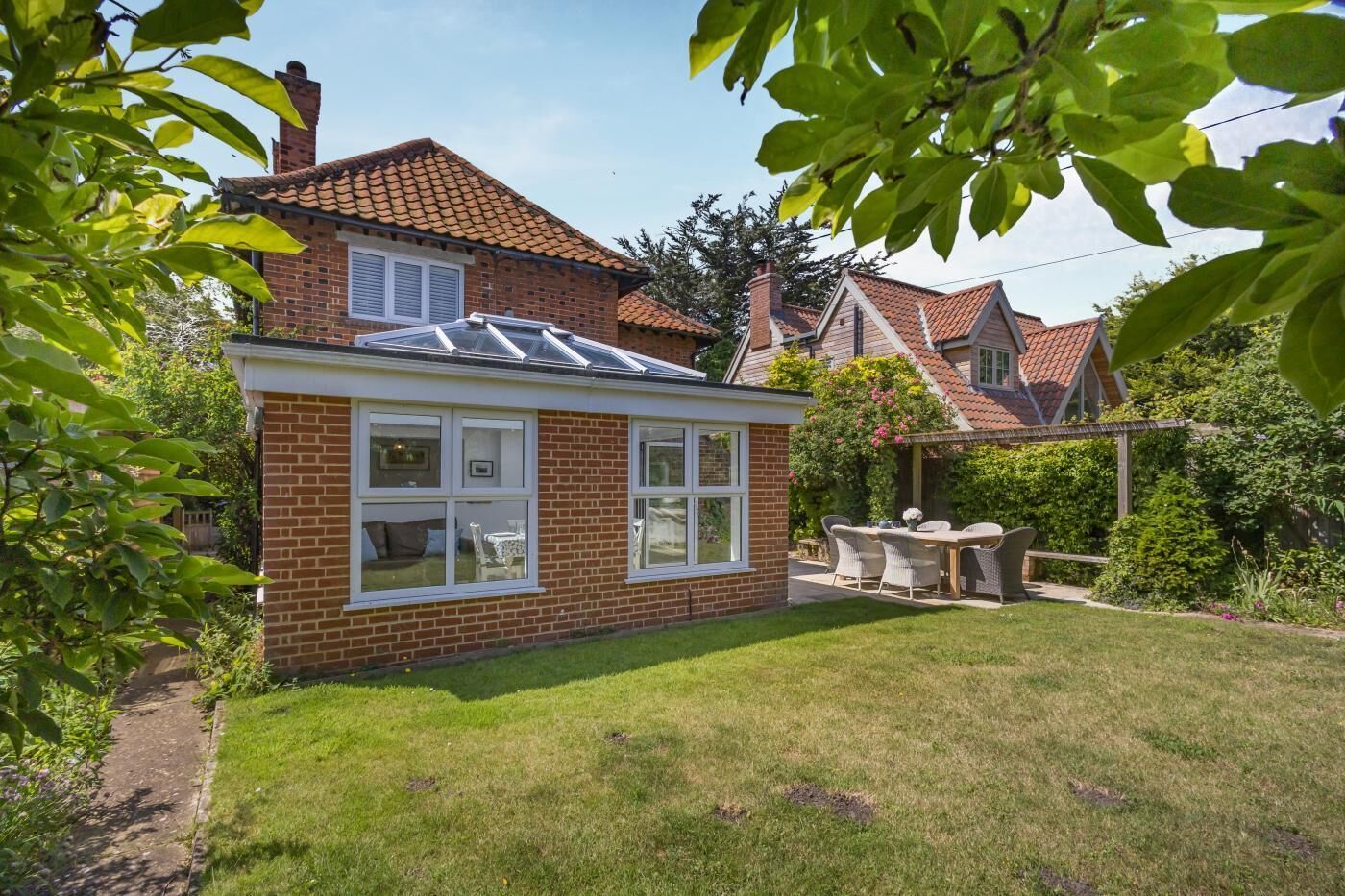 Een bakstenen huis met een zonnedoek, een tuin en een terras met tuinmeubilair.