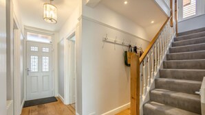 A hallway with a wooden staircase, a door with glass panels, and a coat rack with items. - 3 Bed in Reydon (oc-brae) (Reydon)