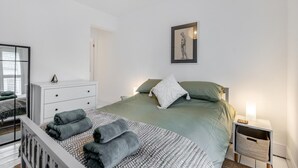 Ein modernes Schlafzimmer mit einem Bett, Nachttischen, einer Kommode und einem gerahmten Kunstwerk an der Wand.