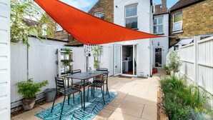 Eine Terrasse mit Tisch und Stühlen, einem weißen Zaun und einem roten Sonnensegel.