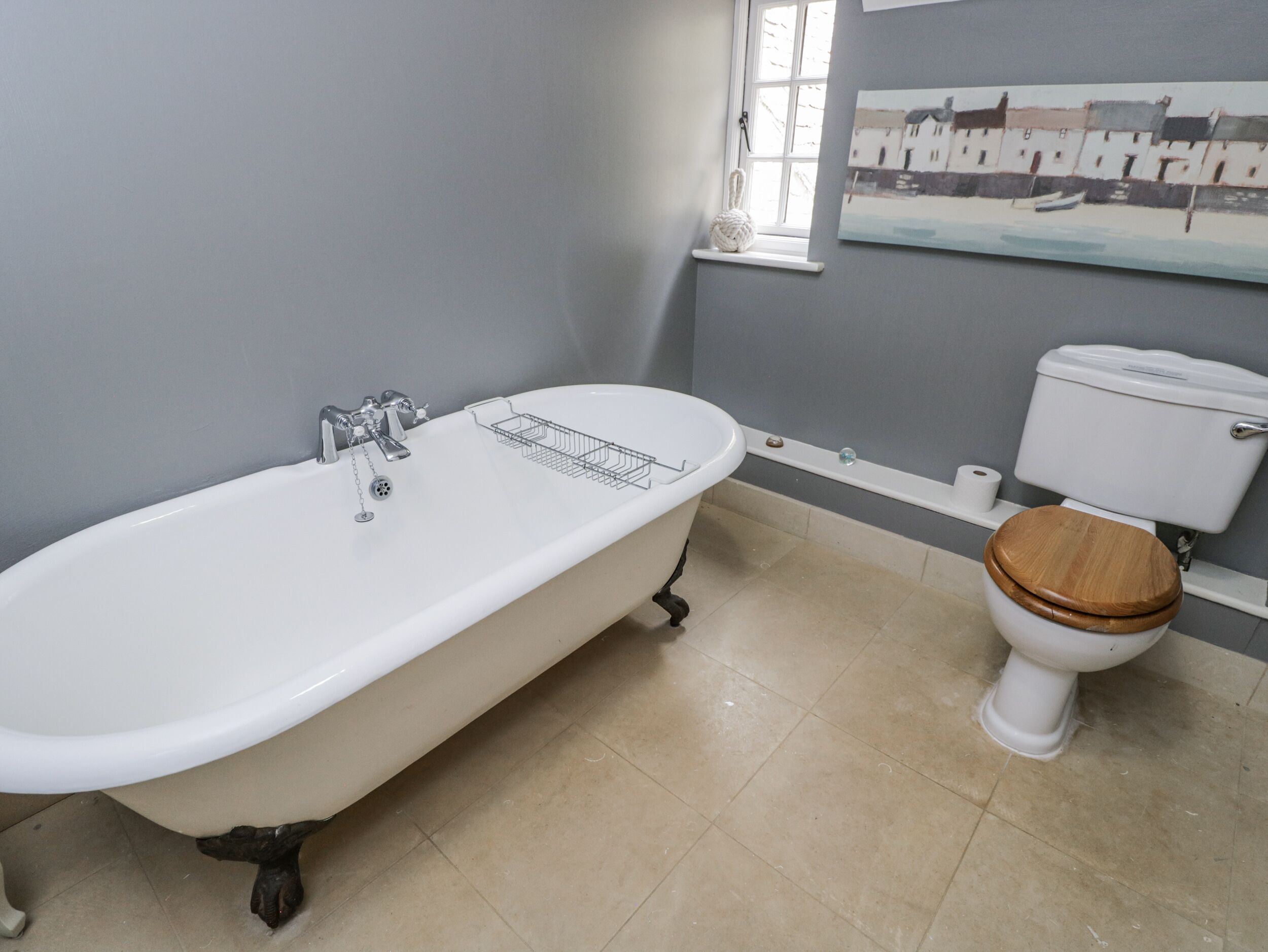 Un baño con una bañera independiente, un inodoro con asiento de madera y una ventana con vistas a la costa.