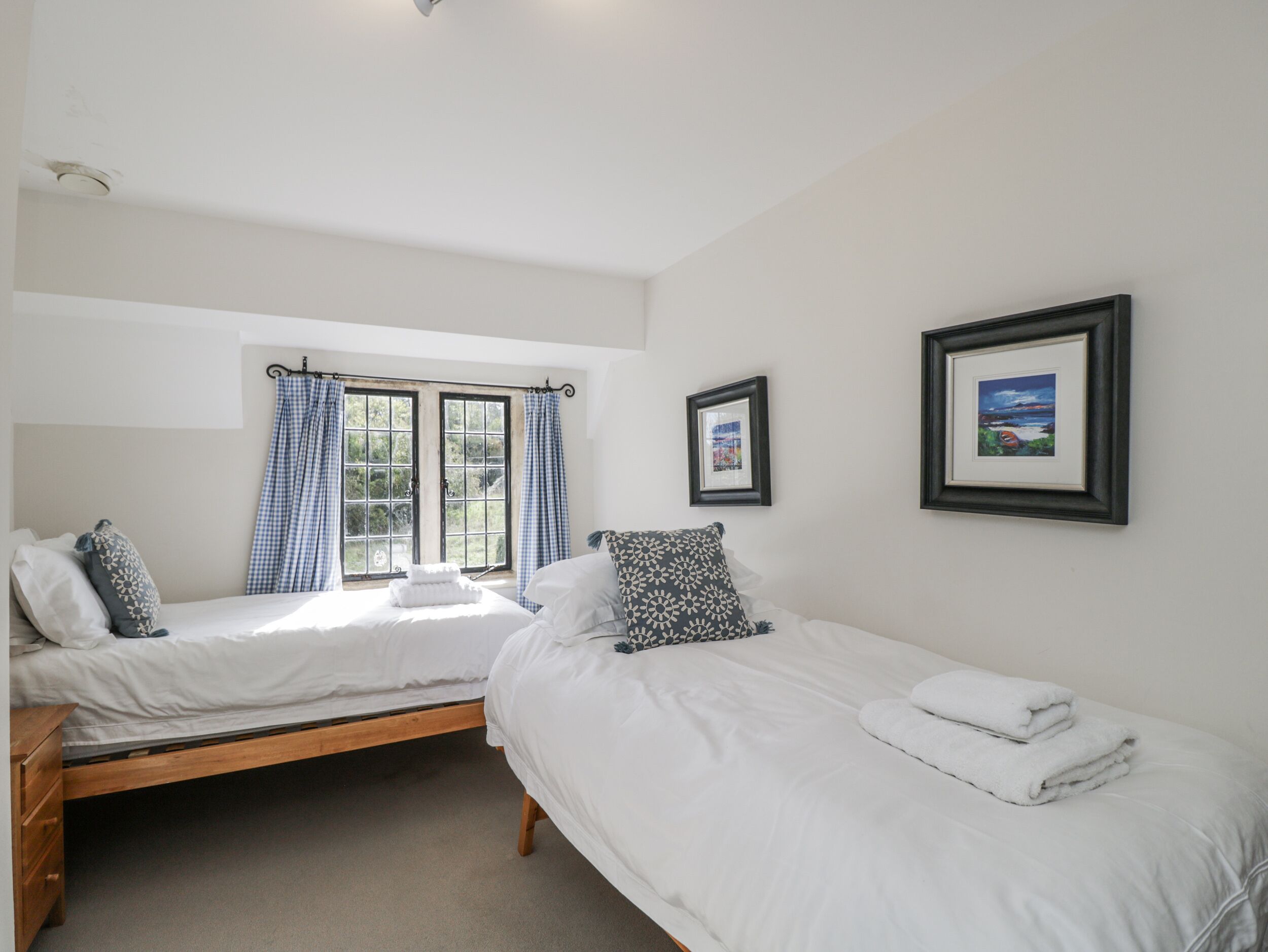 A bedroom with two single beds, a wooden dresser, and a window with curtains.