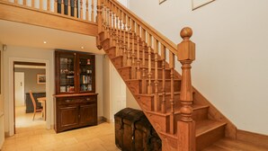 Una escalera de madera con barandilla, un mueble de madera con puertas de cristal y un suelo de baldosas.