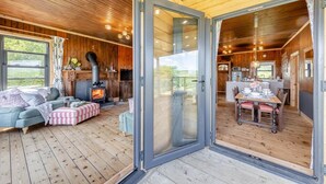 A cozy cabin with a fireplace, a dining area, and a large sliding glass door leading to an outdoor deck. - 3 Bed in Barmouth (oc-c31942) (Barmouth)