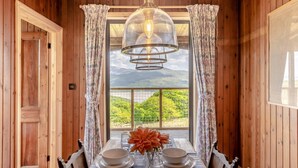 A dining area with a table set for four, a large window with curtains, and a view of greenery and mountains. - 3 Bed in Barmouth (oc-c31942) (Barmouth)