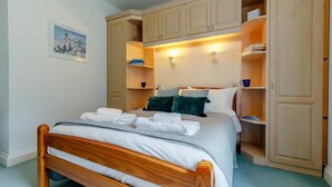 Ein ordentlich bezogenes Bett mit weißen Leinen und einem Holzkopfstück, flankiert von integrierten Holzbögen mit Büchern und Dekorationselementen.