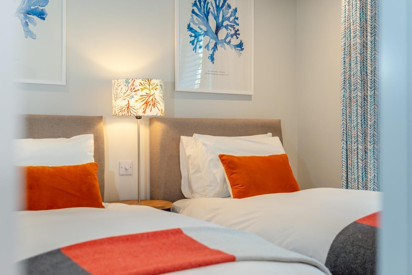 A hotel room with two beds, a nightstand, a lamp, and artwork on the walls.