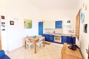 Uma cozinha compacta com armários azuis, uma mesa de jantar de madeira e uma geladeira pequena.