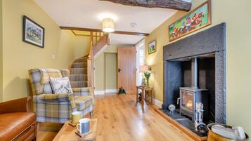A cozy living room with a plaid armchair, a leather sofa, a wooden coffee table, and a fireplace.