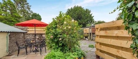Une terrasse avec des meubles d’extérieur, un parasol rouge et une clôture en bois.