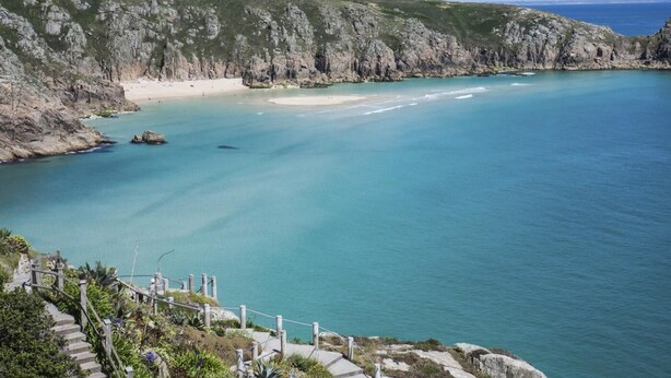 Un paisaje costero con vista despejada al mar, una playa de arena y acantilados rocosos.