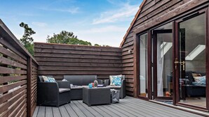 Een terras buiten met rieten meubels en een glazen deur naar de binnenruimte.