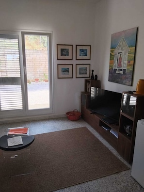 A living room with a sliding glass door, a flat-screen TV, a fireplace, and framed pictures on the wall. - Country house in an olive grove, 8 km from the Ionian Sea (Bernalda)