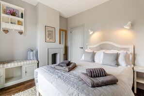 A bedroom with a bed, bedside tables, a dresser, a fireplace, and wall-mounted lighting. - 5 Bed in Walberswick (oc-lev) (Walberswick)