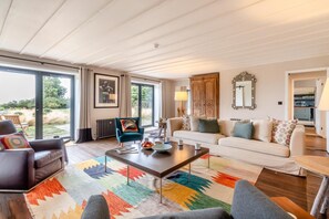 Ein geräumiges Wohnzimmer mit großem Fenster, einer Couch, einem Couchtisch und einem Sessel.