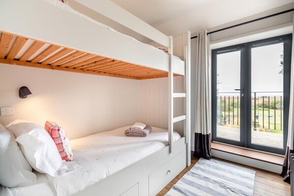 Una habitación con literas, un escritorio pequeño, una ventana con cortinas y vistas al exterior.