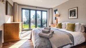 A hotel room with a large bed, a wooden dresser, a nightstand, a lamp, and a framed picture on the wall. - 5 Bed in Walberswick (oc-lev) (Walberswick)