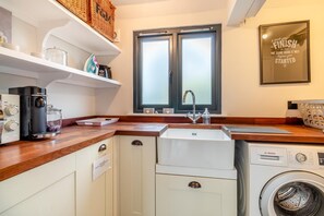 A compact kitchen with a washing machine, a coffee maker, and a window with frosted glass. - 5 Bed in Walberswick (oc-lev) (Walberswick)