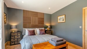 Un dormitorio moderno con una cama grande, cabecera de madera, mesitas de noche con lámparas y un banco de madera con toallas.