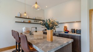 Una cocina moderna con una isla central, taburetes de bar, un florero de madera con flores y diversos electrodomésticos de cocina.