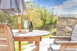 Una mesa de madera al aire libre con una botella de Prosecco, un vaso de agua y un plato de comida.