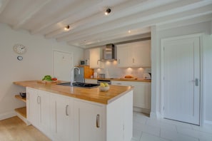 Une cuisine avec des meubles blancs, un plan de travail en bois, un évier et une horloge au mur.