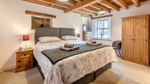 A bedroom with a large bed, wooden beams, a dresser, a wardrobe, and a window with flowers.