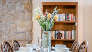 A dining table set with white plates, bowls, and a clear glass vase with flowers.