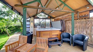 Un patio al aire libre con mobiliario de madera, un jacuzzi y vistas al jardín.