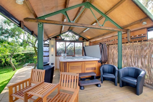 An outdoor patio area with wooden furniture, a hot tub, and a view of the garden.