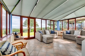 A spacious sunroom with large windows, a sectional sofa, and a dining area.